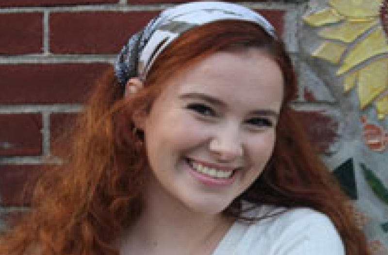 A young woman smiling while standing against a brick wall.